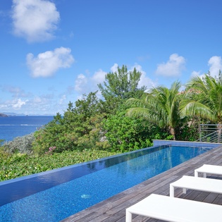 Infinity pool overlooking tropical paradise with pristine blue waters and lush palm trees.