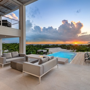 Modern luxury villa featuring an infinity pool and panoramic sunset views across tropical landscape.