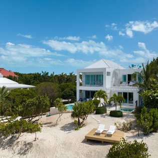 Modern beachfront villa with swimming pool nestled among tropical palms and native vegetation on pristine white sand.