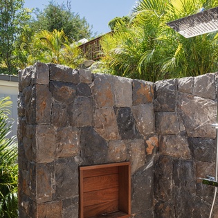 Rinse off under cascading water in your private stone-walled outdoor shower, surrounded by tropical palms and open sky.