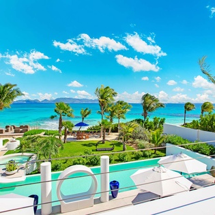 A luxurious beachfront resort featuring stunning turquoise waters, lush tropical landscaping with swaying palms, and pristine outdoor amenities beneath a brilliant Caribbean sky.