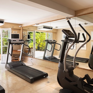 The fitness center overlooks lush tropical greenery through floor-to-ceiling windows, bringing natural light into your workout space with modern cardio equipment and free weights.