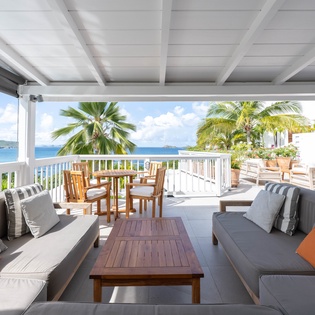 Your private oceanfront terrace invites relaxation with plush seating and sweeping sea views framed by swaying palms.