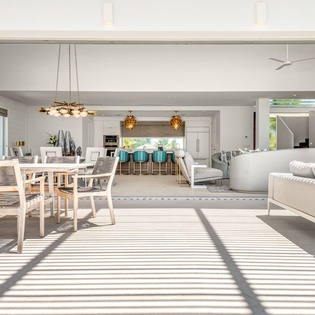 Relax in your stunning open-plan living space where natural light streams through floor-to-ceiling windows, creating beautiful shadow patterns across sleek modern furnishings.