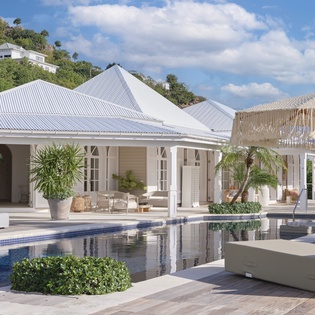Elegant tropical villa with pristine pool and thatched umbrella, nestled among lush hillside gardens in an exclusive Caribbean setting.