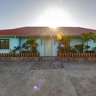 Charming turquoise cottage with tropical palms and welcoming wooden fence creates an inviting island retreat.