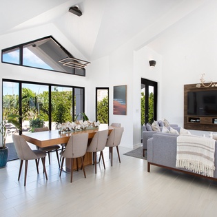 Bright, airy living and dining area with soaring vaulted ceilings and floor-to-ceiling windows framing lush tropical views. Relax in modern comfort as natural light fills your open-plan retreat.