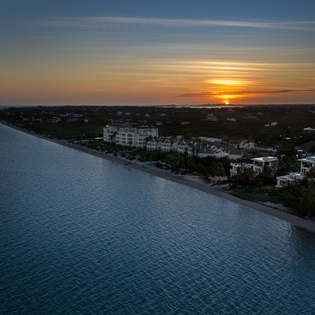 Aerial view of coastal properties with pristine beach and dramatic sunset over the horizon.