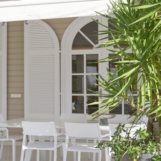 Your private patio offers a serene escape with comfortable white seating surrounded by lush tropical greenery and elegant French doors.