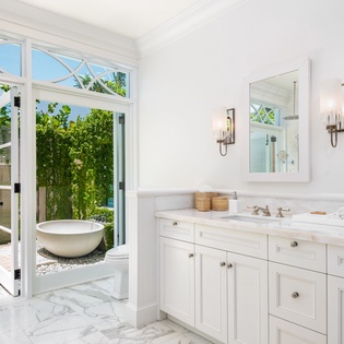 Elegant marble bathroom with double vanities opens to your private outdoor sanctuary, complete with a luxurious soaking tub surrounded by lush greenery and natural light.
