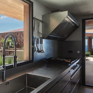 Cook with stunning ocean views through floor-to-ceiling windows in this sleek modern kitchen with professional-grade appliances and tropical surroundings.