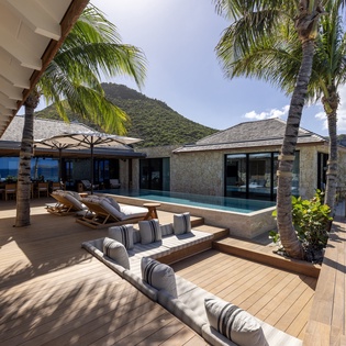 Luxurious beachfront villa featuring pristine white sand beach, swaying palm trees, and stunning mountain backdrop creating the perfect tropical paradise.