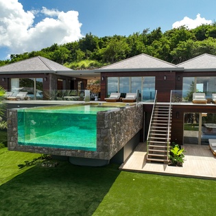 Modern luxury villa featuring elevated infinity pool, tropical gardens, and multiple terraces surrounded by lush hillside vegetation.