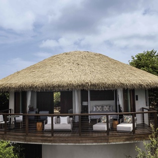 Tropical villa featuring natural thatched roof and spacious deck surrounded by lush jungle foliage.