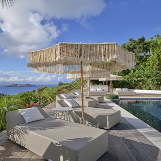 A stunning oceanfront pool deck surrounded by lush tropical gardens and pristine blue waters stretching to distant islands.