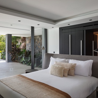 Wake up in your luxurious suite with tropical garden views and seamless indoor-outdoor living through expansive glass doors.