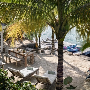 Your private beach paradise awaits with swaying palms, soft sand loungers, and kayaks ready for adventure.