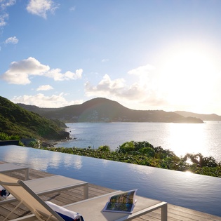 Infinity pool overlooking pristine coastline with mountains and islands creating a stunning tropical backdrop.