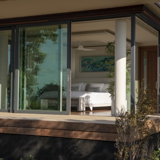 Floor-to-ceiling windows frame your serene bedroom retreat, where tropical breezes meet modern comfort in this elevated sanctuary.