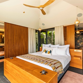 Step into your serene bedroom suite with vaulted ceilings, warm wood accents, and lush tropical garden views just beyond your window—a peaceful retreat designed for rest and relaxation.