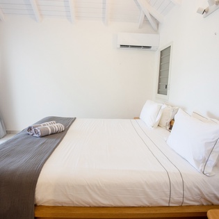 Slip into crisp white linens beneath exposed wooden beams in your serene bedroom retreat, where modern comfort meets coastal charm.