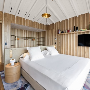 Relax in your stylish bedroom featuring warm wood walls, crisp white linens, and modern amenities for the perfect peaceful retreat.