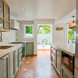 Your fully-equipped kitchen blends modern style with tropical charm. Sleek marble countertops, stainless steel appliances, and glass-front cabinets create a bright, functional space where you can prepare meals while gazing at lush palm trees through large 