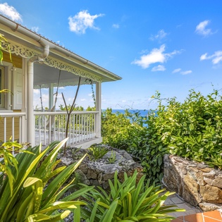Charming property building surrounded by lush tropical gardens with stunning sea views beyond the verdant landscape.
