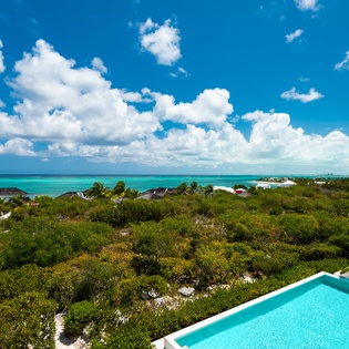 Aerial view showcasing pristine turquoise waters, lush tropical landscape, and crystal-clear pool deck surrounded by vibrant Caribbean scenery.