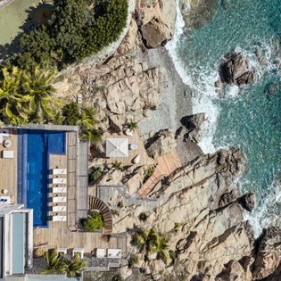 Stunning oceanfront property with private pool deck overlooking turquoise waters and rocky coastline.