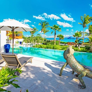 A luxurious villa with a stunning turquoise pool, lush palm gardens, and oceanfront views—ideal for relaxing under the Caribbean sun.