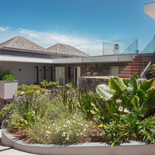 Modern tropical villa featuring contemporary architecture surrounded by lush landscaping and stunning glass-walled rooftop terrace under clear Caribbean skies.