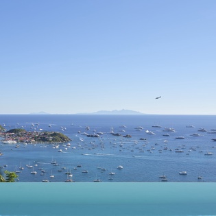 Stunning infinity pool overlooks a pristine harbor filled with boats and distant mountain views across crystal-clear Caribbean waters.