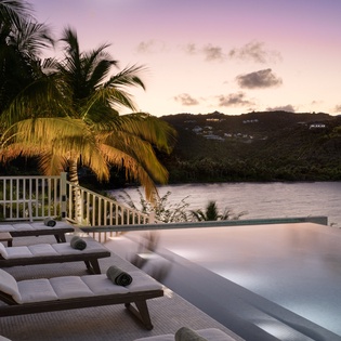 Tropical paradise with infinity pool overlooking pristine waters as sunset paints the sky in soft pastels.