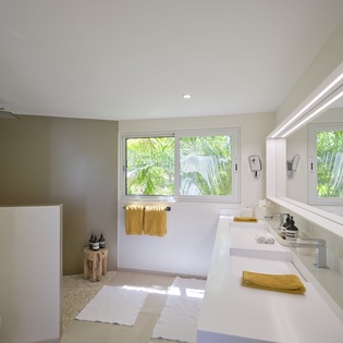 Soak away your cares in this bright, spa-inspired bathroom, where natural light and lush garden views create a peaceful sanctuary. Clean lines and warm touches—like the golden towels and rain shower—invite you to truly unwind.