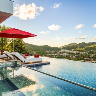 Spectacular infinity pool overlooking tropical mountains and coastline, offering panoramic views during golden hour lighting.