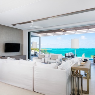 Sink into plush white sofas as ocean breezes drift through your open terrace doors, framing endless turquoise waters in your personal paradise.