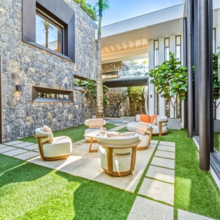Your private courtyard oasis features modern seating surrounded by lush greenery and striking stone walls.