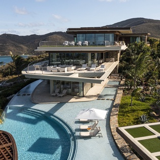 Modern luxury villa with curved pool and stunning mountain-sea views in a tropical Caribbean setting.