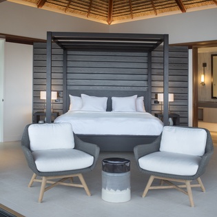 Retreat to your elegant suite with modern four-poster bed, cozy seating area, and soaring bamboo ceiling that creates a serene tropical sanctuary.