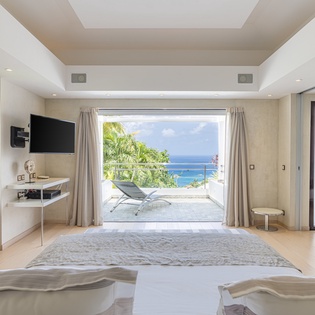 Step into your serene bedroom suite and soak in the breathtaking ocean views framed by open doors. Palm trees sway in the breeze as your private balcony beckons you to unwind and savor paradise.