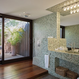 Immerse yourself in this stunning mosaic-tiled bathroom where spa-like luxury meets your private outdoor oasis through expansive glass doors.