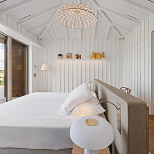 Your serene bedroom sanctuary features crisp white linens and exposed beams, with stunning views beckoning through floor-to-ceiling windows.