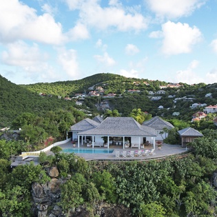 Stunning hillside villa showcasing elegant architecture nestled among lush tropical mountains and neighboring homes.