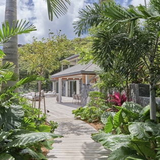 A tropical villa nestled in lush gardens, surrounded by swaying palms and vibrant plants in this island paradise setting.