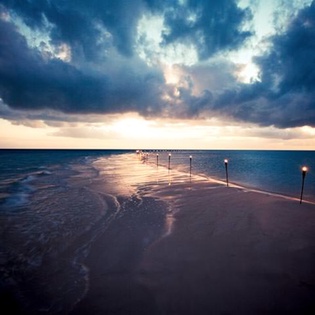 Dramatic clouds part over an illuminated waterfront pier extending into calm waters.