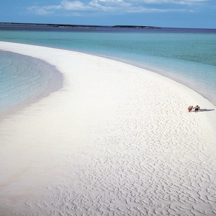 Pristine white sand beach stretches into crystal-clear turquoise waters under bright blue skies, creating a perfect tropical paradise.