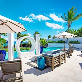 A luxurious poolside oasis features modern loungers, shaded seating areas, and striking architectural details framed by swaying palms and brilliant blue skies—your perfect tropical escape.