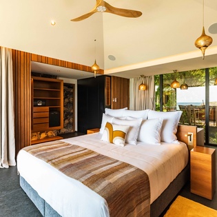 Slip into crisp linens and soak in the natural light streaming through floor-to-ceiling windows, where warm wood tones and elegant pendant lighting create your serene retreat.