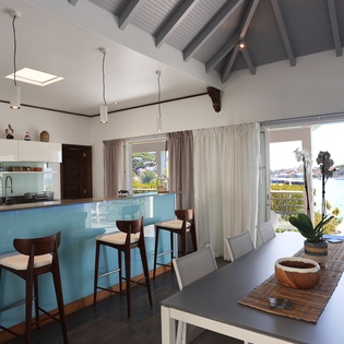Your open-plan kitchen and dining area frames stunning ocean views through floor-to-ceiling windows, creating the perfect tropical gathering space.